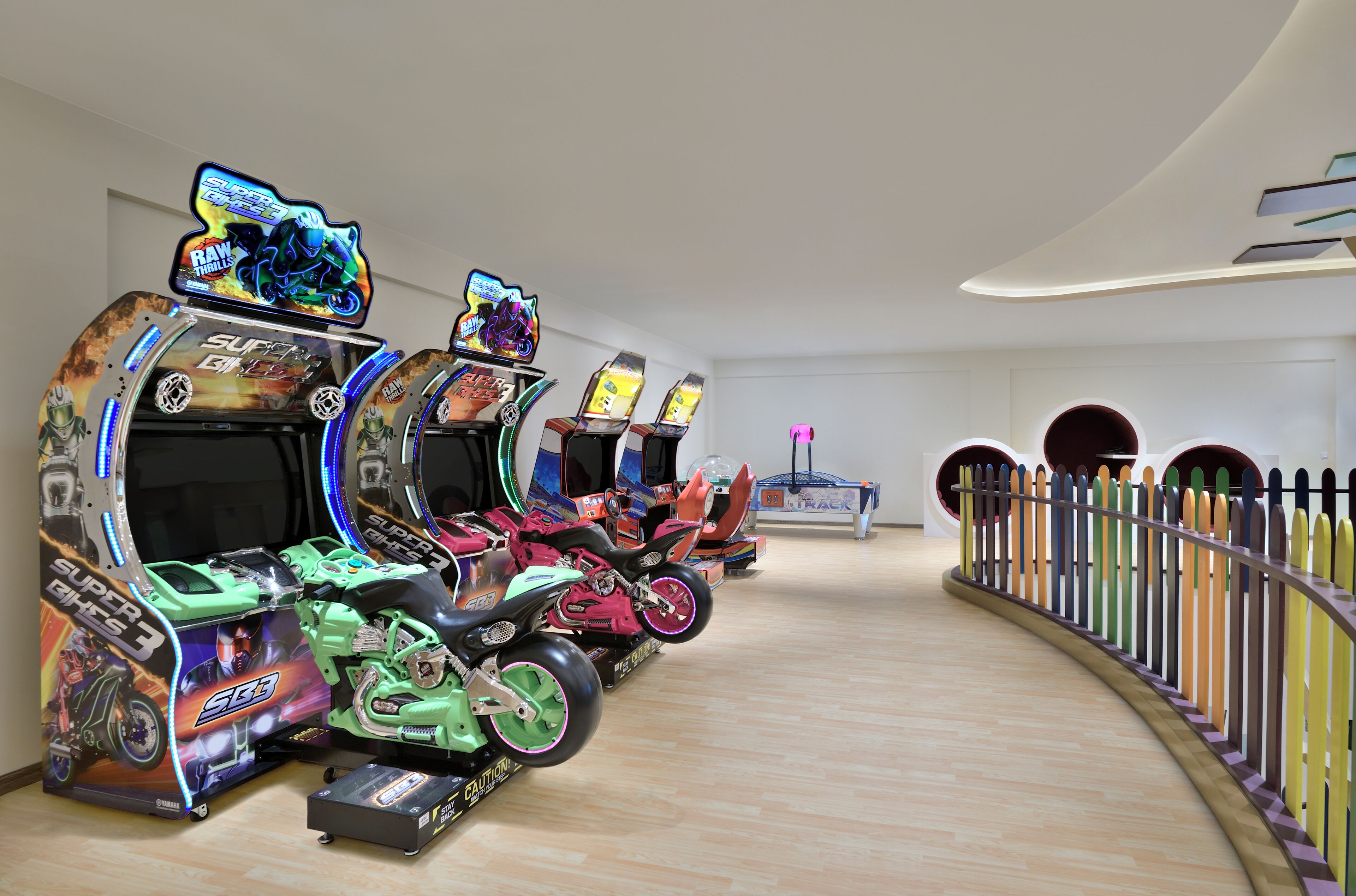 Una fila de máquinas de videojuegos de estilo recreativo con diseños coloridos y una barrera de madera curvada con orificios circulares.