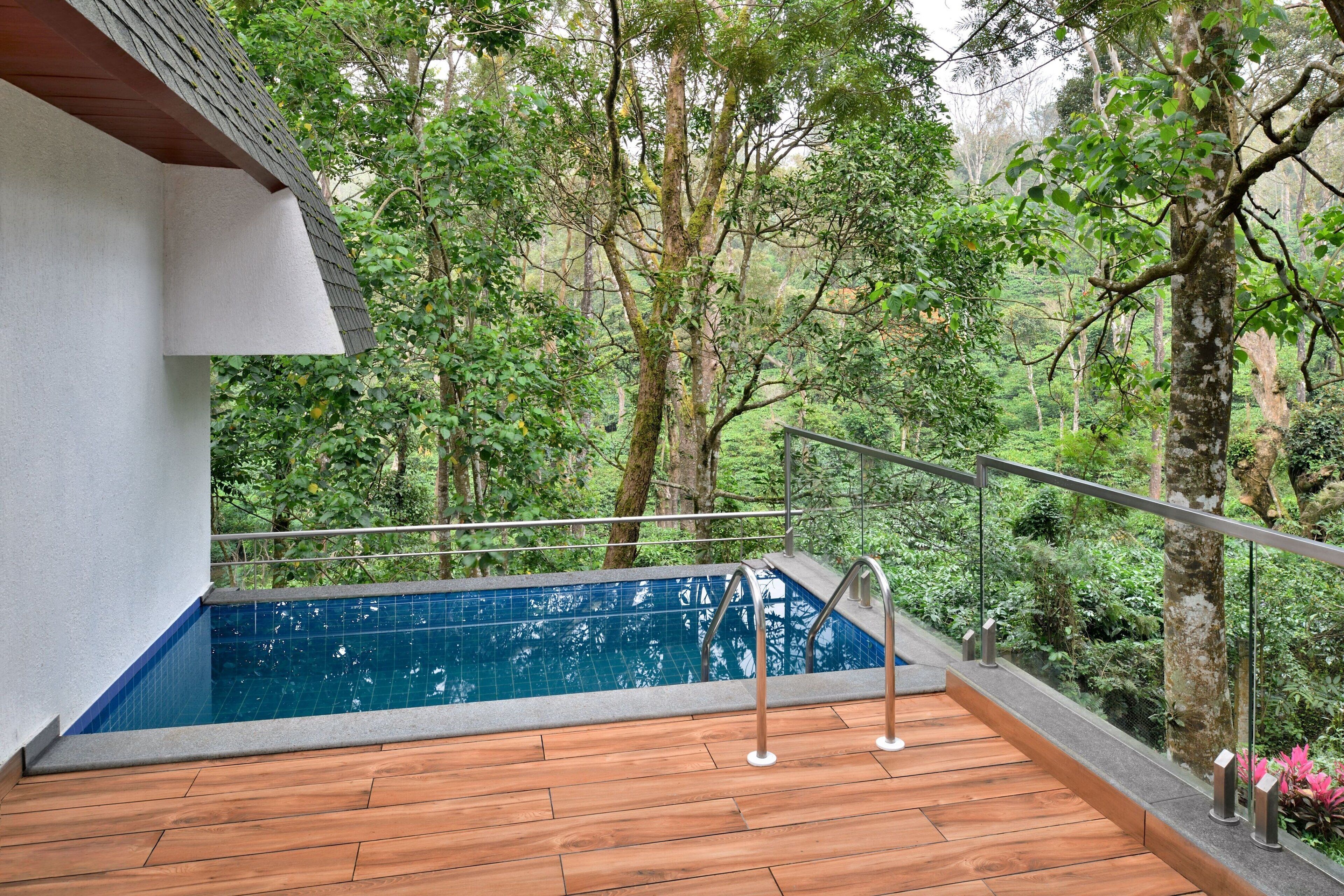 A pool with a wooden deck and metal railings, surrounded by lush greenery.