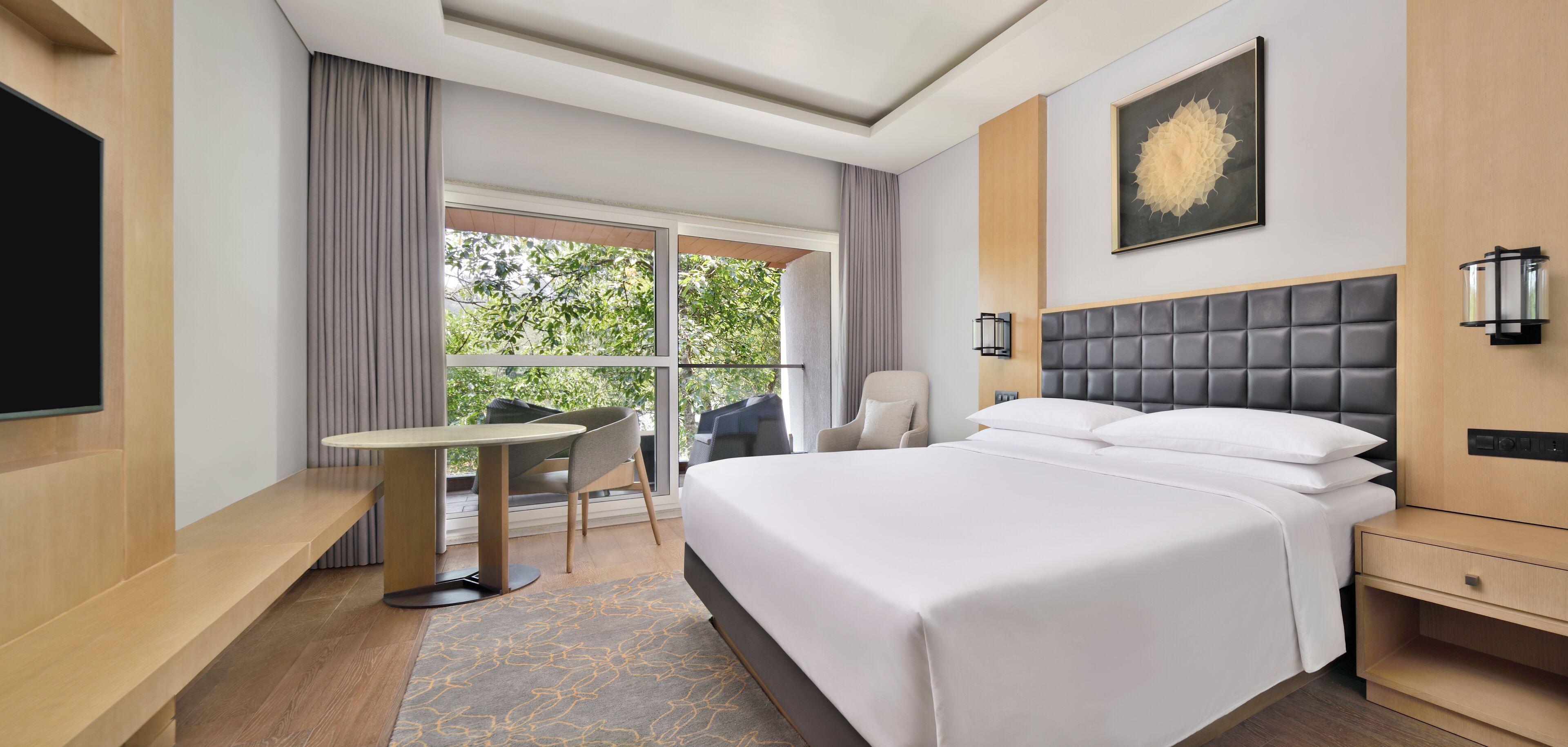 Ein Hotelzimmer mit einem großen Bett, einem Schreibtisch, einem Sessel, einem Fernseher und einem Fenster mit Vorhängen.
