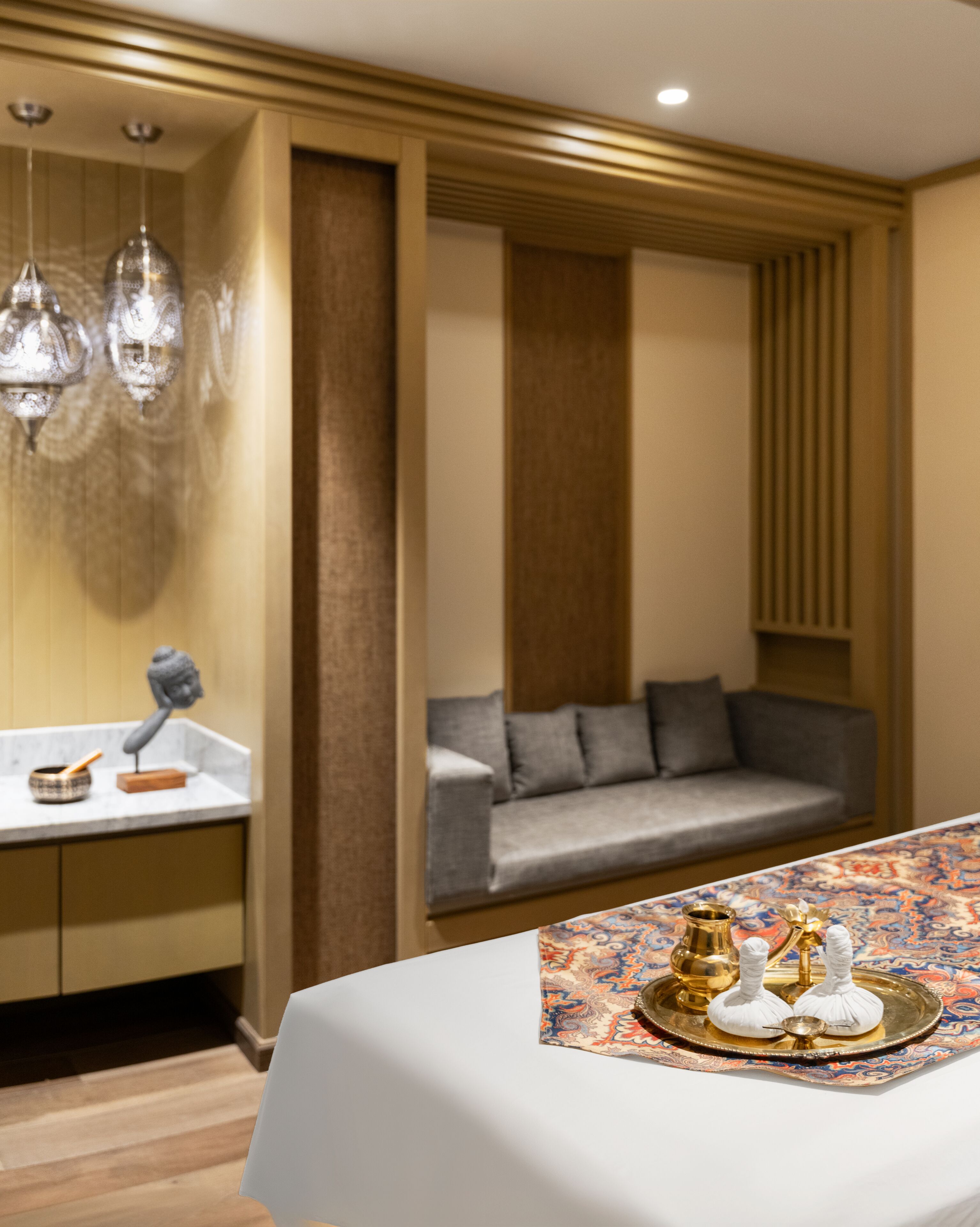 Une chambre d’hôtel moderne avec un canapé, une table à manger agrémentée d’un plateau d’objets décoratifs, un lustre et un mur revêtu de panneaux en bois.