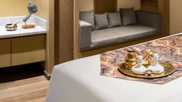 Une chambre d’hôtel moderne avec un canapé, une table à manger agrémentée d’un plateau d’objets décoratifs, un lustre et un mur revêtu de panneaux en bois.