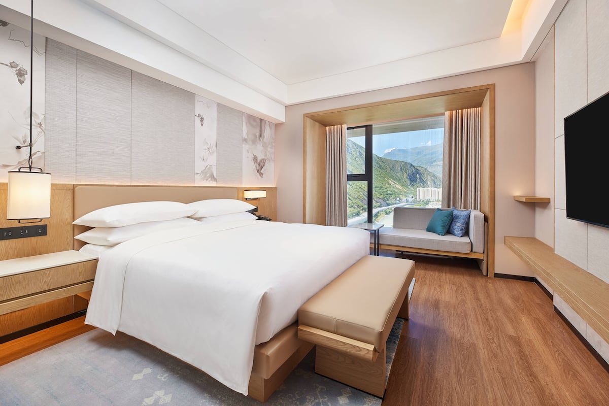 Une chambre d’hôtel moderne avec un grand lit, un banc, un canapé et une télévision.
