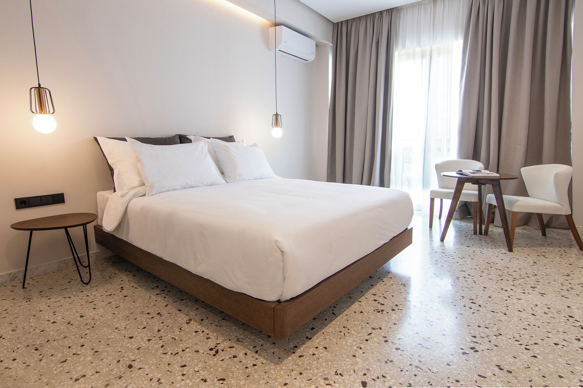 Una habitación de hotel moderna con una cama grande, una mesita pequeña, una silla y un escritorio.