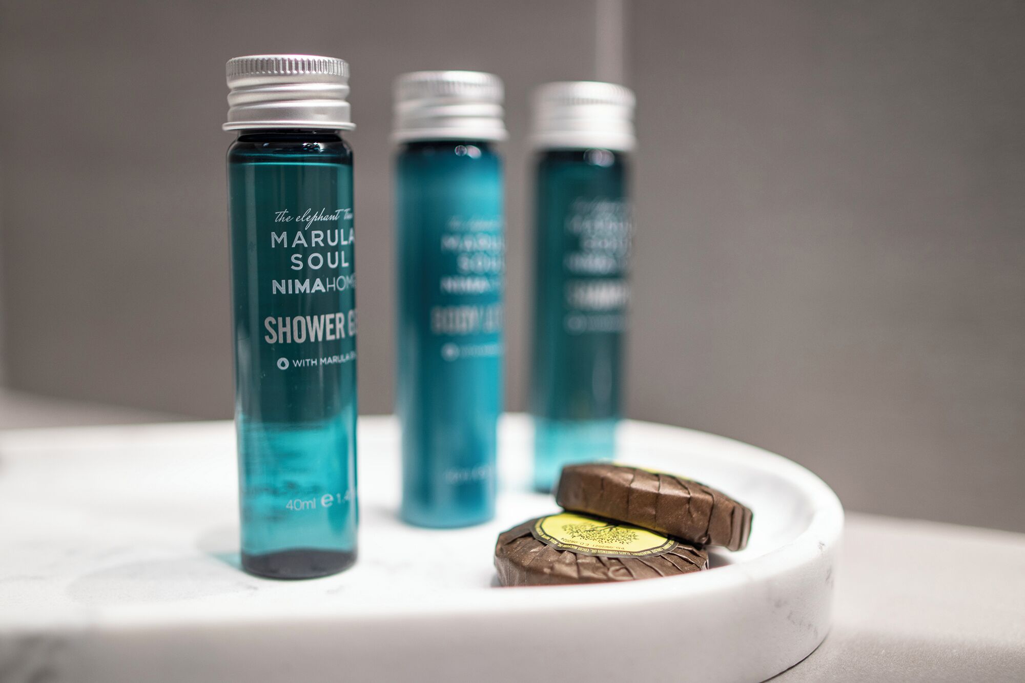 Three bottles of 'The Elephant Marula Soul NimaHom Shower Gel' on a white surface.