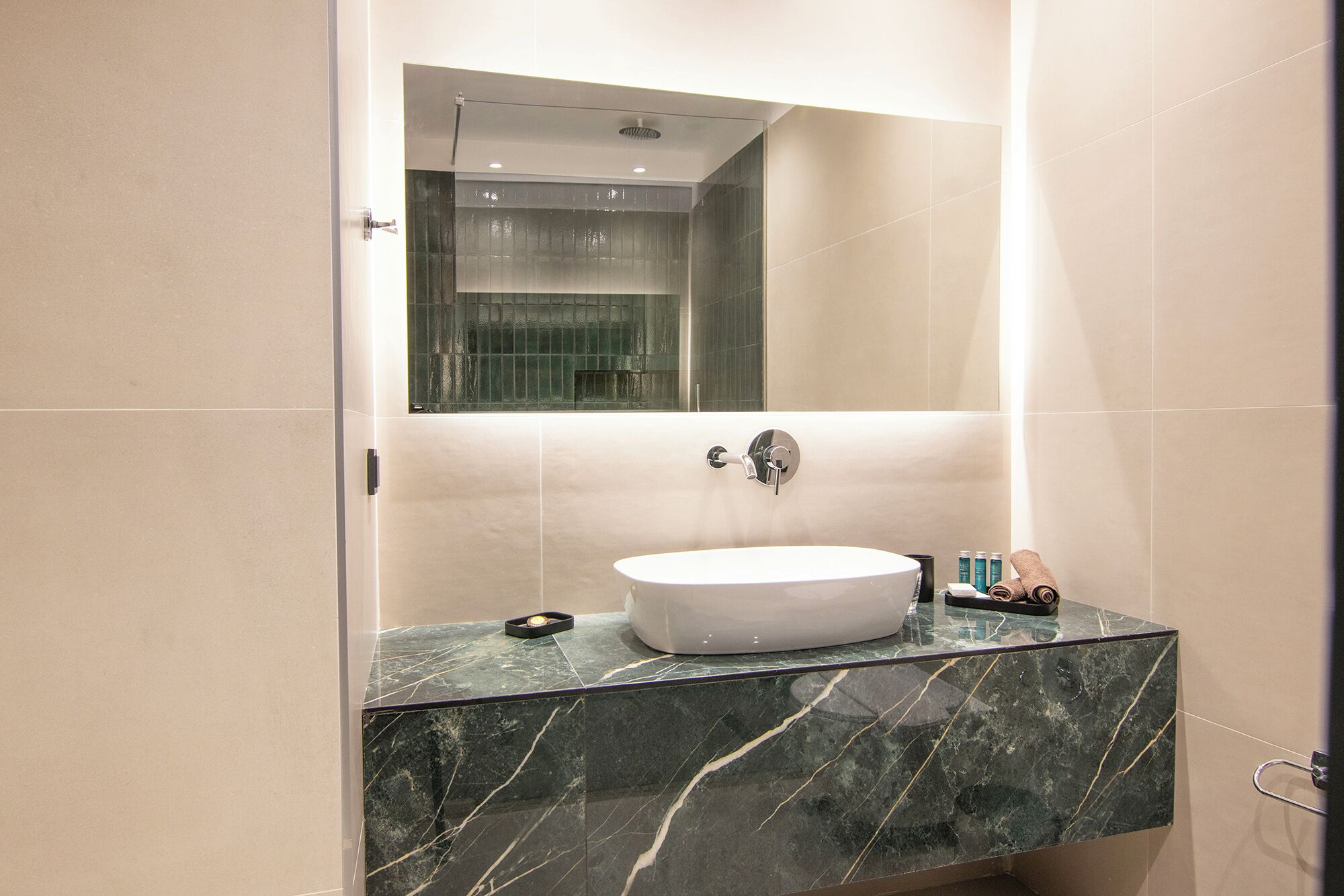 Un baño con tocador de mármol, lavamanos blanco y espejo encima.