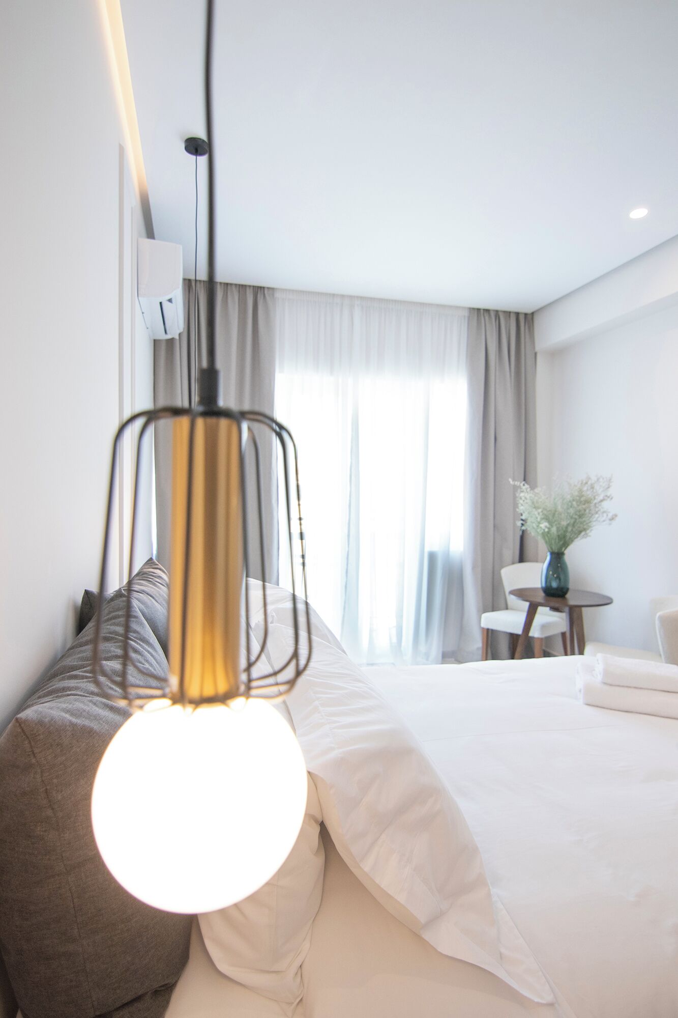 Una habitación de hotel moderna con una cama grande, una mesita de noche con un florero y una lámpara colgante.