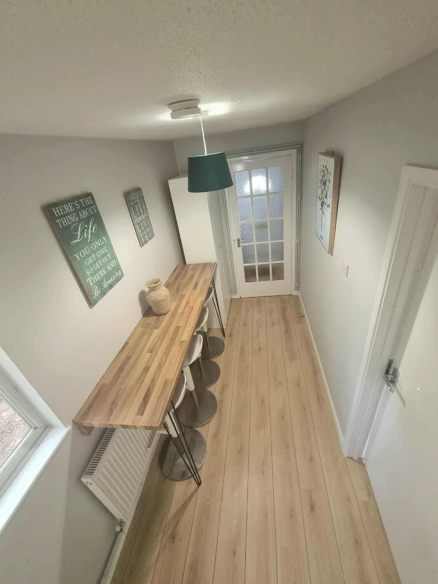 A narrow hallway with a wooden table and chairs, a radiator, and a door with frosted glass panels.