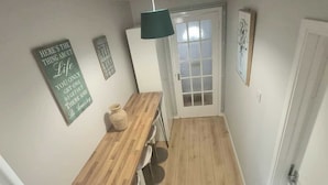 Un pasillo estrecho con una mesa de madera y sillas, un radiador y una puerta con paneles de vidrio esmerilado.