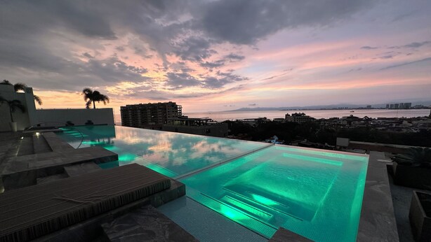 An infinity pool with a view of the city and sunset.