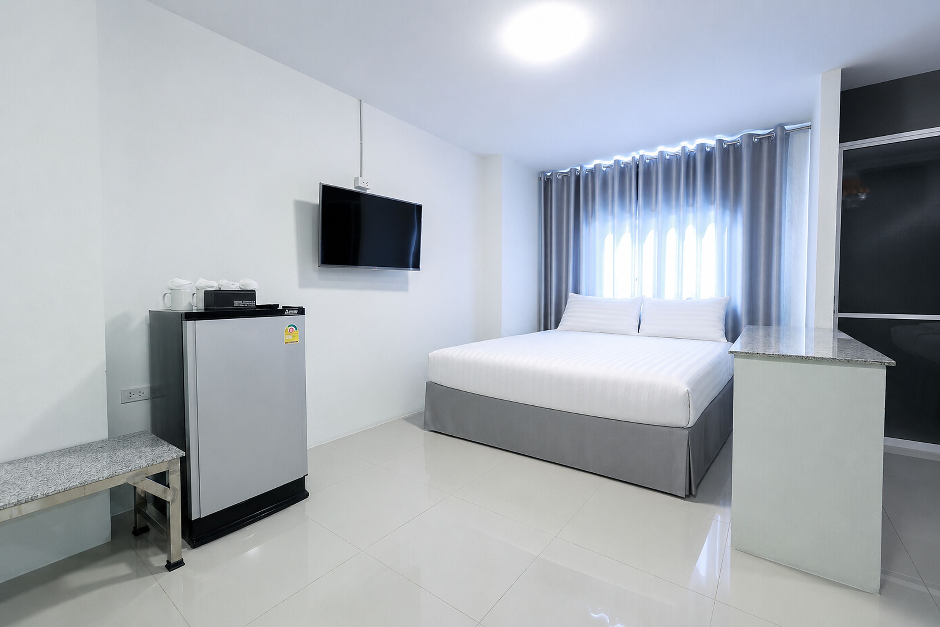 Ein Hotelzimmer mit einem Bett, einem an der Wand befestigten Fernseher, einem Kühlschrank und einem Fenster mit Vorhängen.
