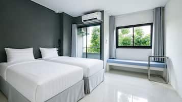 A modern hotel room with two beds, a large window with a view of greenery, and an air conditioning unit.