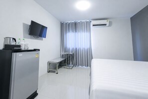 Quarto de hotel com cama, escrivaninha, televisão, frigorífico e ar condicionado.