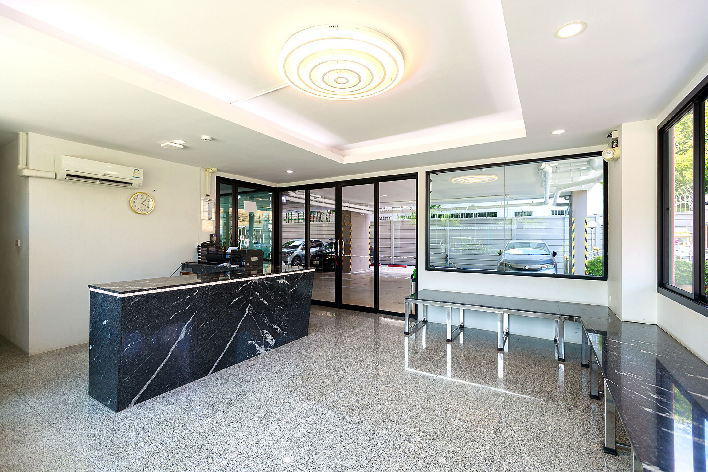 A modern reception area with a marble counter, glass doors leading outside, and a ceiling with circular lighting.