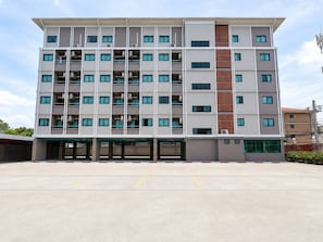 Un hotel de varios pisos con fachada plana, numerosas ventanas y un estacionamiento al frente.