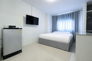 A hotel room with a bed, a television mounted on the wall, a refrigerator, and a window with curtains.