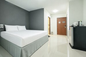 Habitación de hotel con cama, puerta, refrigerador y una mesita con tetera y tazas.
