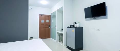 Habitación de hotel con cama, televisor montado en la pared, refrigerador y puerta que da a otra habitación.