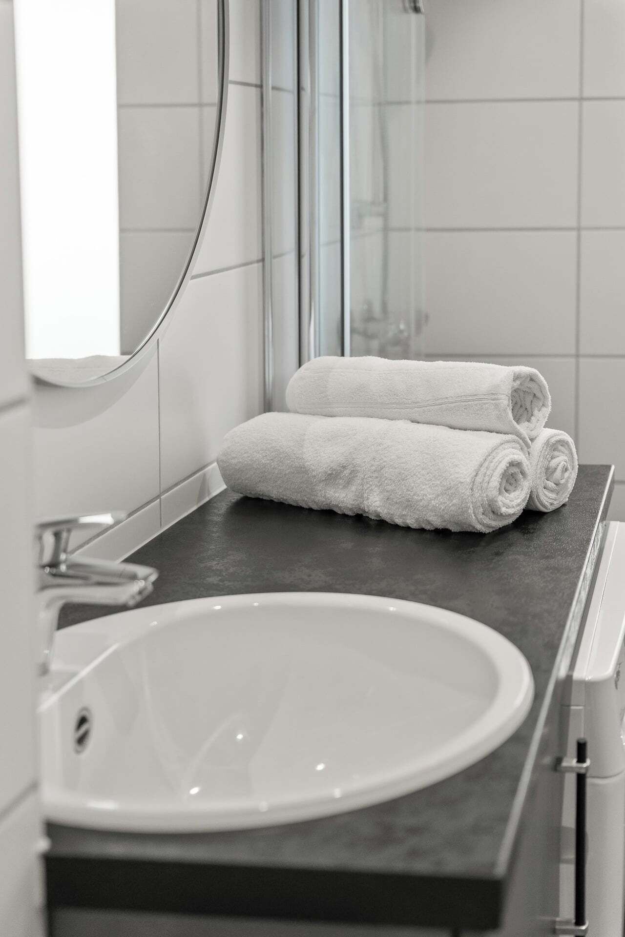 A bathroom with a white sink, a dark countertop, and two rolled white towels.
