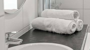 Un baño con un lavamanos blanco, una encimera oscura y dos toallas blancas enrolladas.