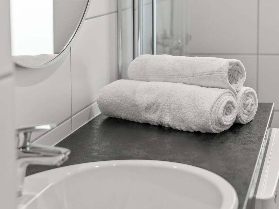 A bathroom with a white sink, a dark countertop, and two rolled white towels.