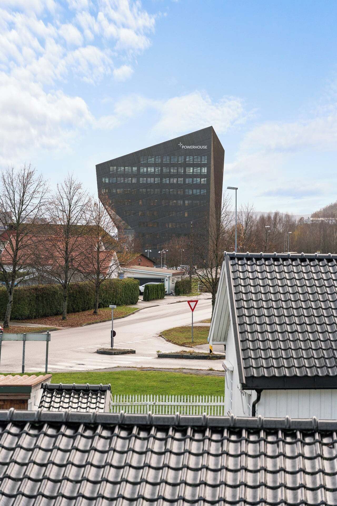 A modern building with a unique angular design, a clear sky, and a residential area with tiled roofs and a white picket fence.