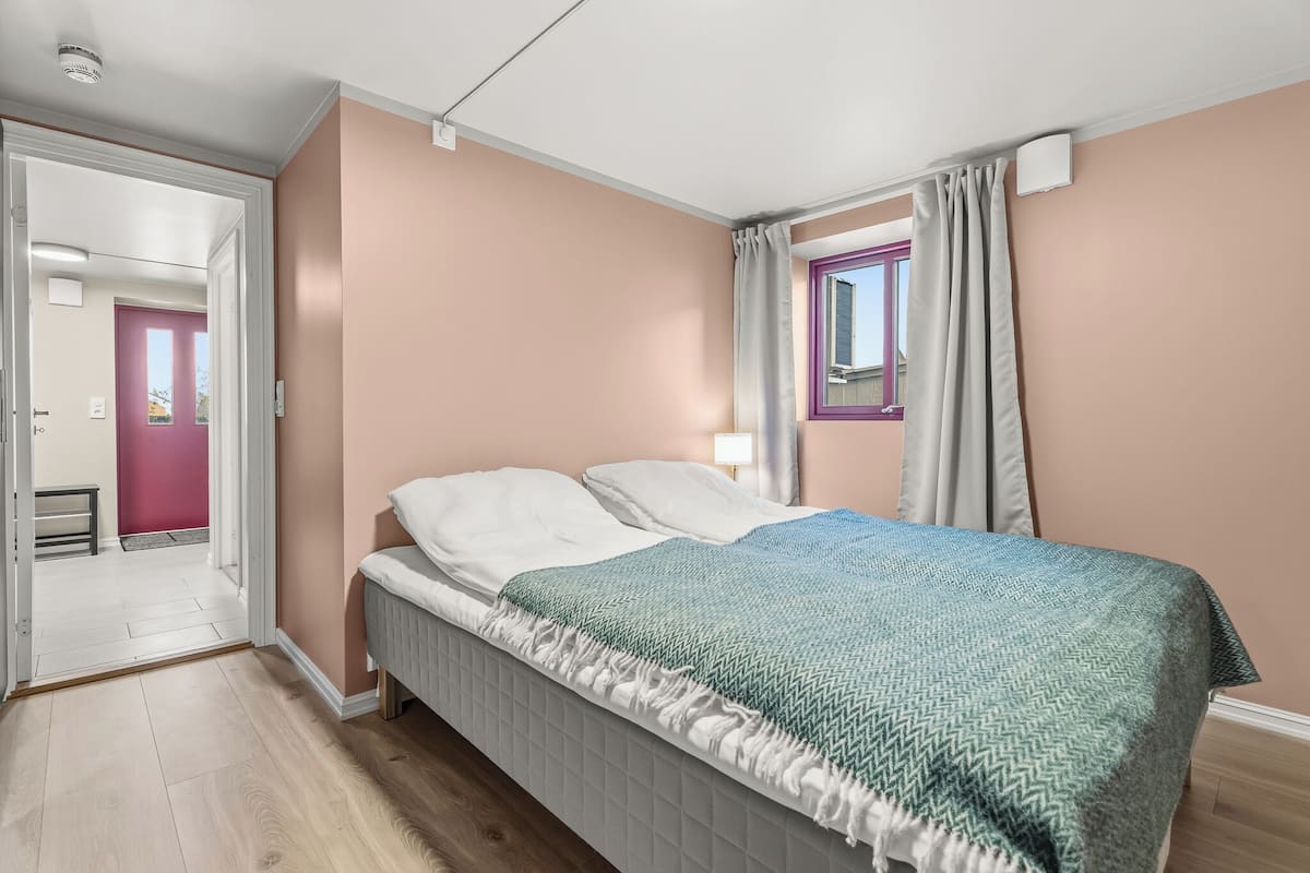 Ein Schlafzimmer mit Bett, einem Fenster mit Vorhängen und einer Tür zu einem anderen Raum.