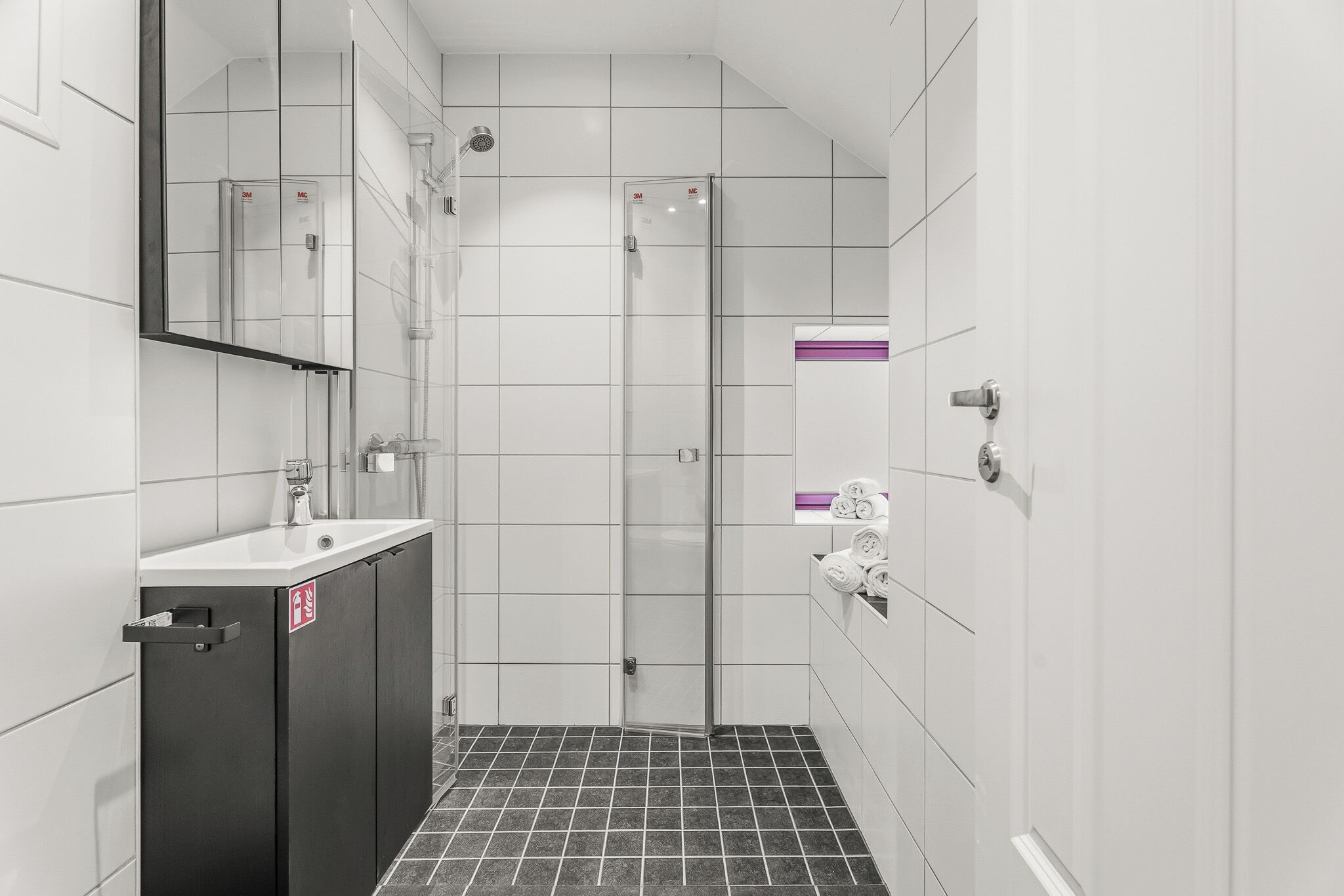Een moderne badkamer met een douchecabine van glas, een wastafel met spiegel en een handdoekrek.