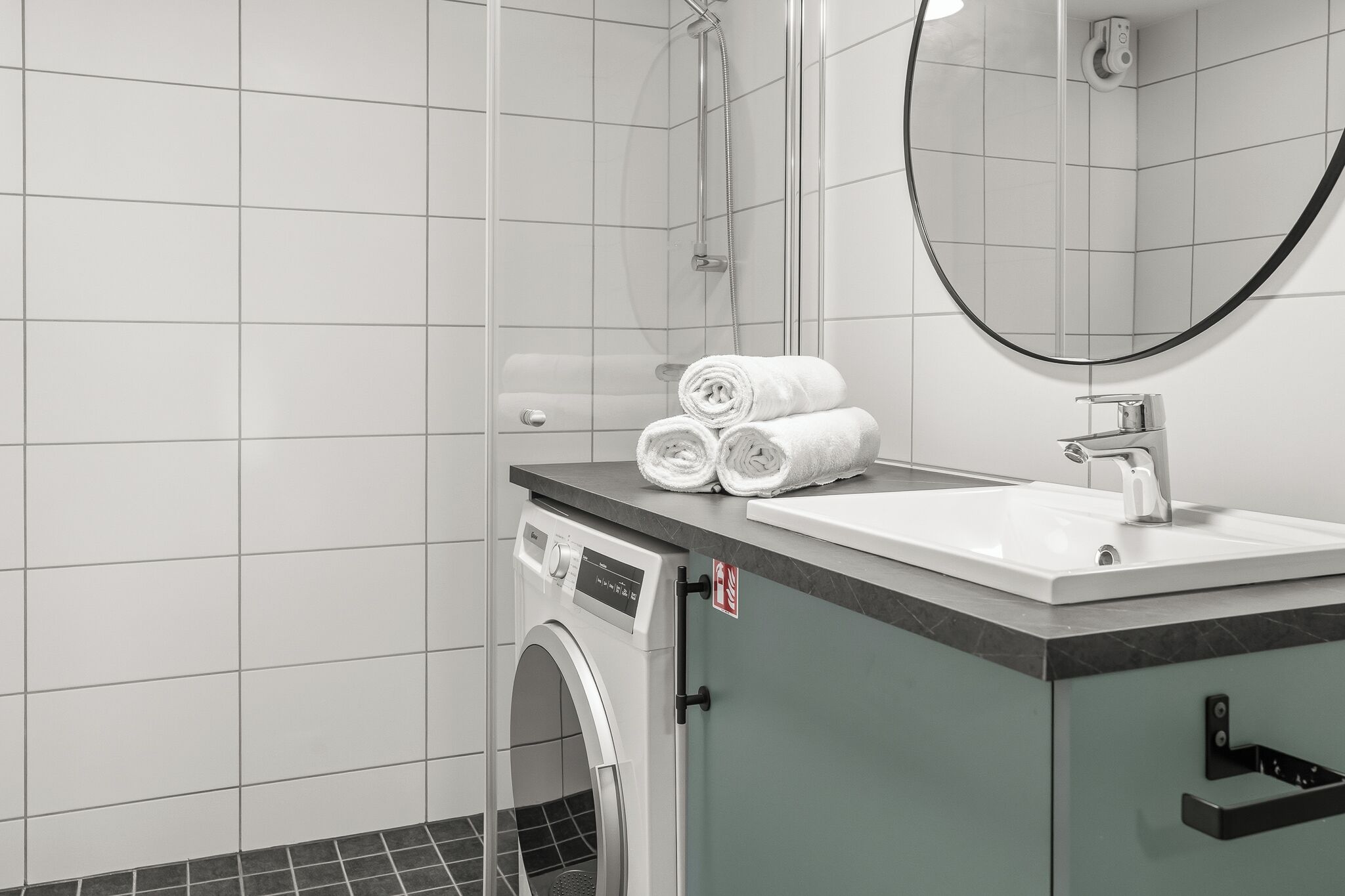 A modern bathroom with a washing machine, a sink, and a mirror.