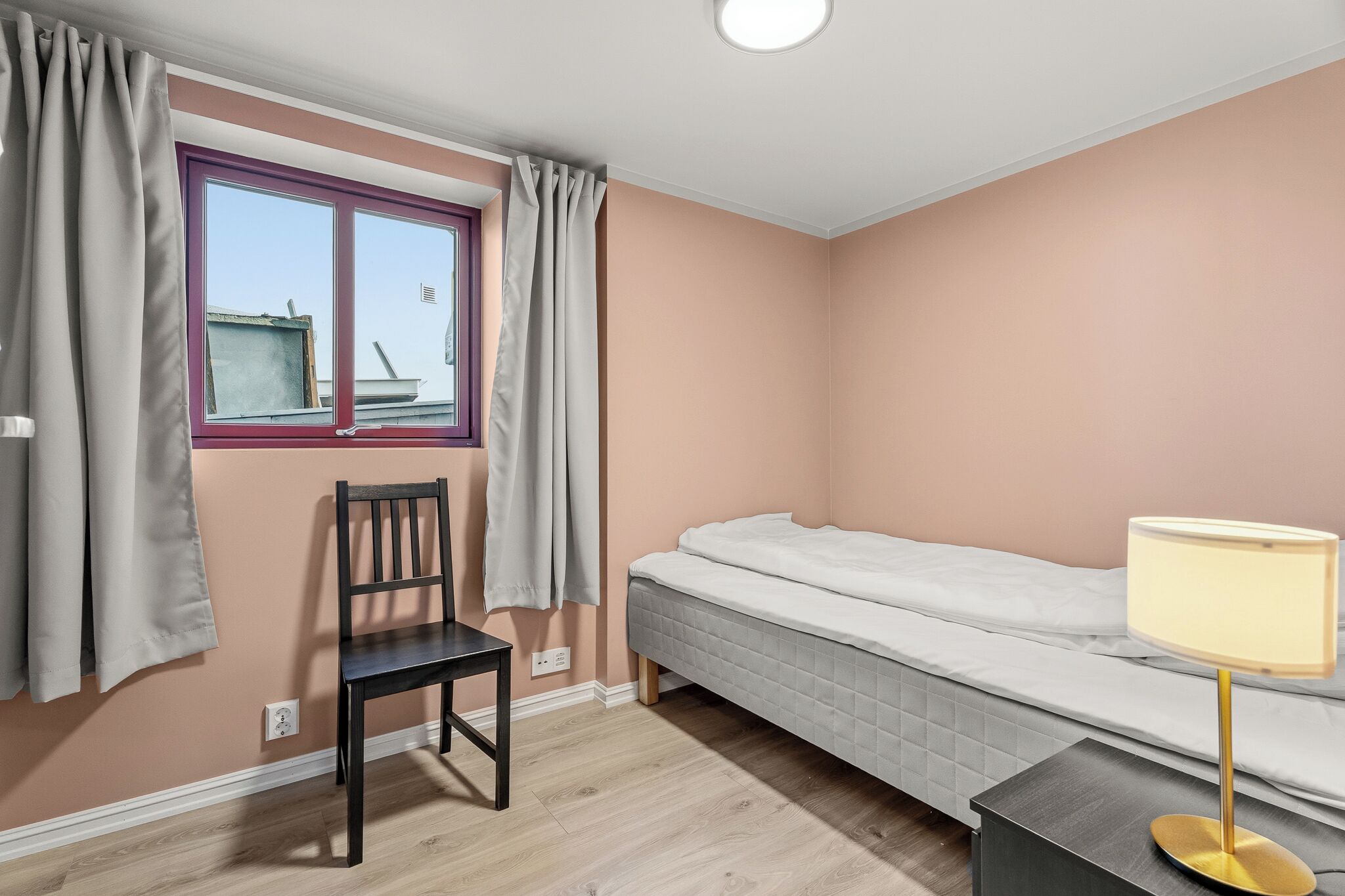A room with a bed, a chair, a table, and a window with curtains.