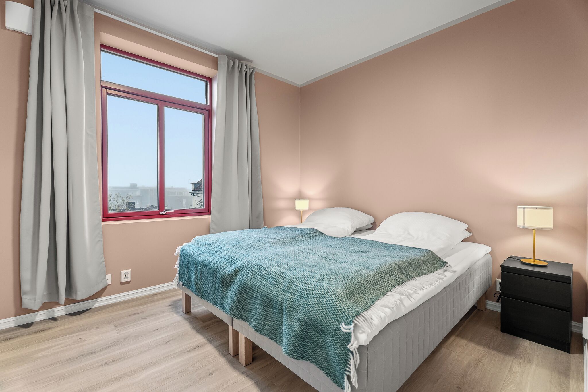 Un dormitorio con cama, lámparas de noche, una ventana con cortinas y vista a la ciudad.