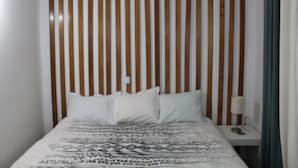 Ein Bett mit gemustertem Bettbezug, einem Lattenrost-Kopfstück und einem Nachttisch mit Lampe.