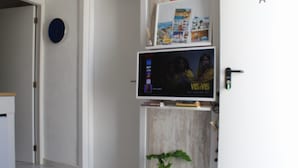 Ein Zimmer mit einem an der Wand befestigten Flachbildfernseher, einer Topfpflanze auf einem Regal und einer Tür mit Griff.