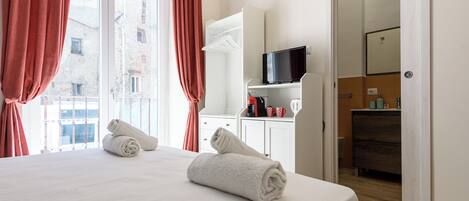 A hotel room with a bed, a television, a bathroom, and a view of buildings outside.