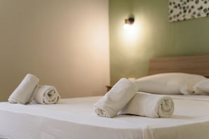 Een net opgemaakt bed met opgerolde witte handdoeken en een wandlamp.