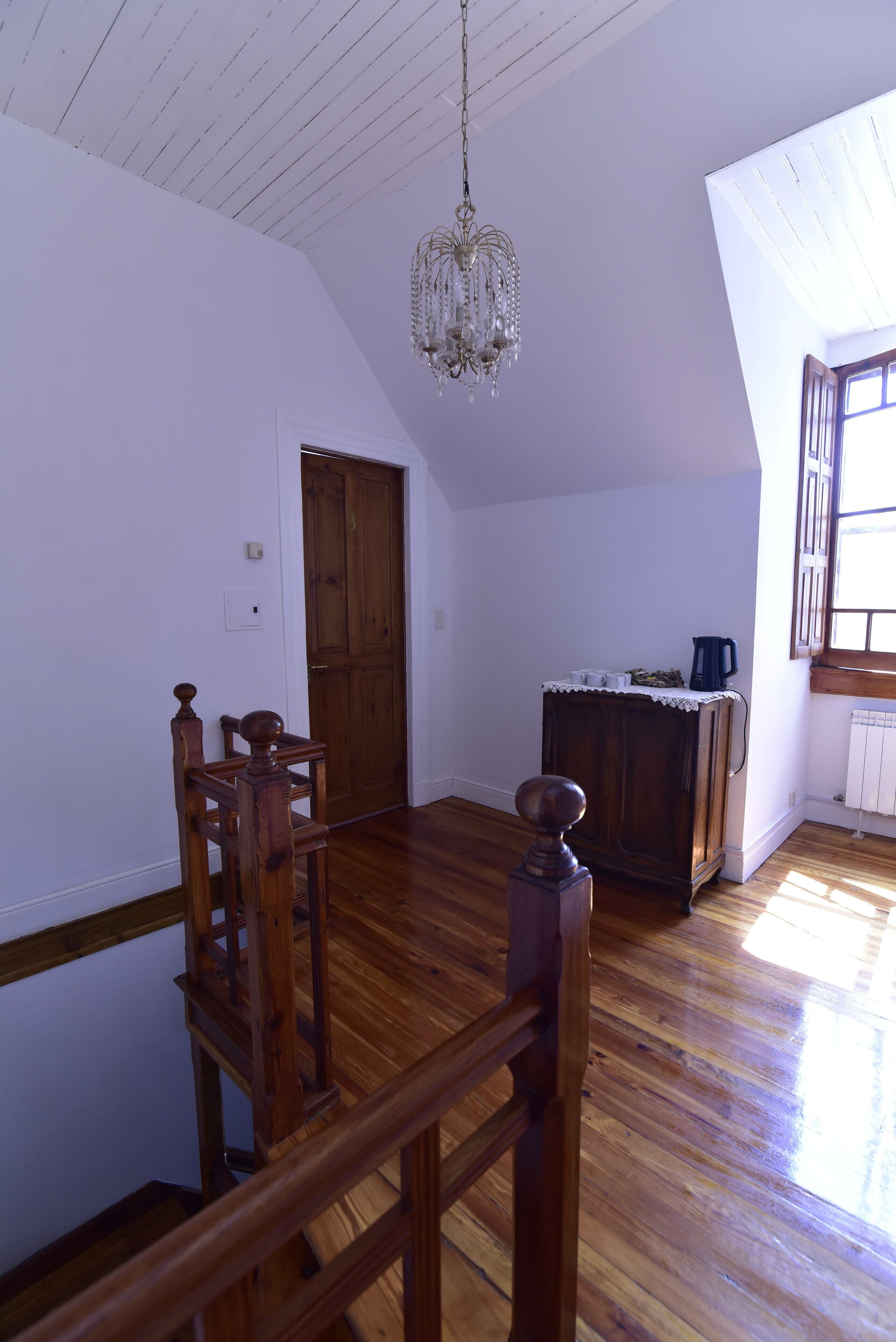 A spacious room with wooden flooring, a chandelier, a wooden door, and a window with a view.