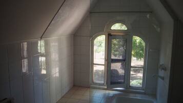 A bathroom with white tiles, a bathtub, and a window with an arched design.