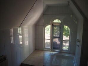 A bathroom with white tiles, a bathtub, and a window with an arched design.