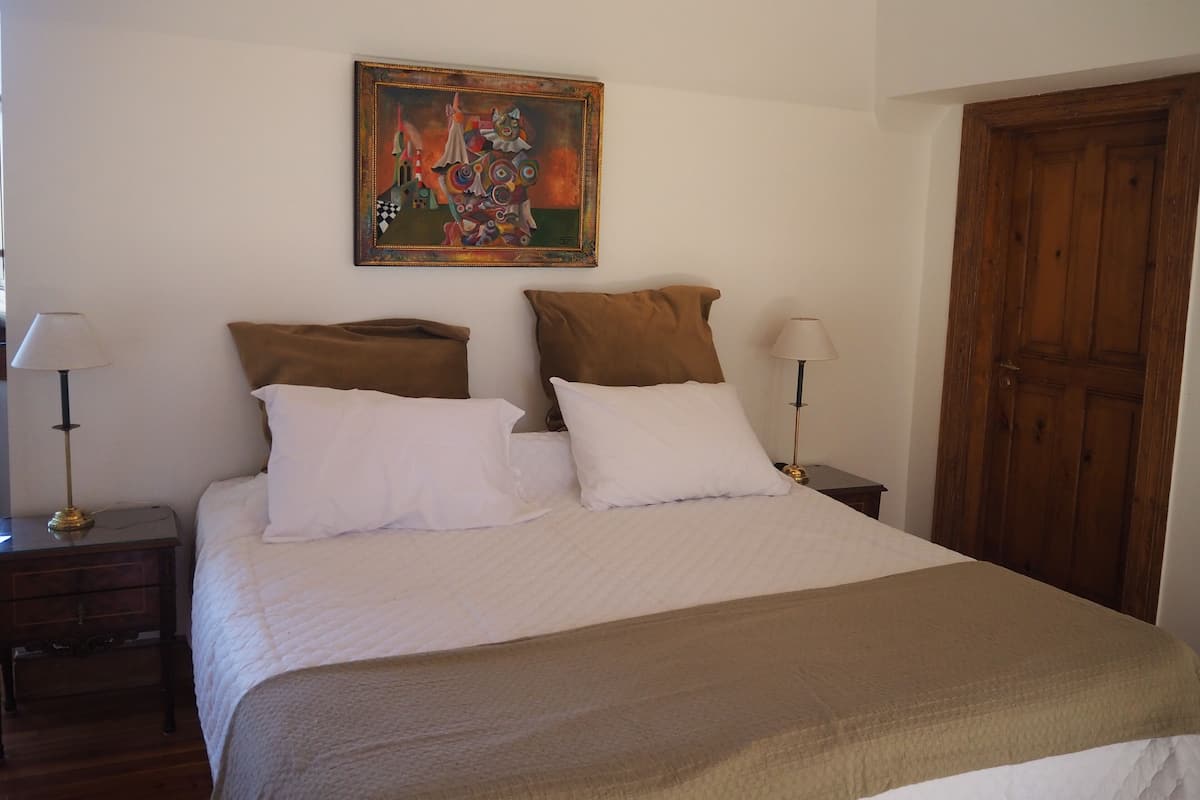 A bedroom with a bed, two nightstands, a wooden door, and a painting on the wall.