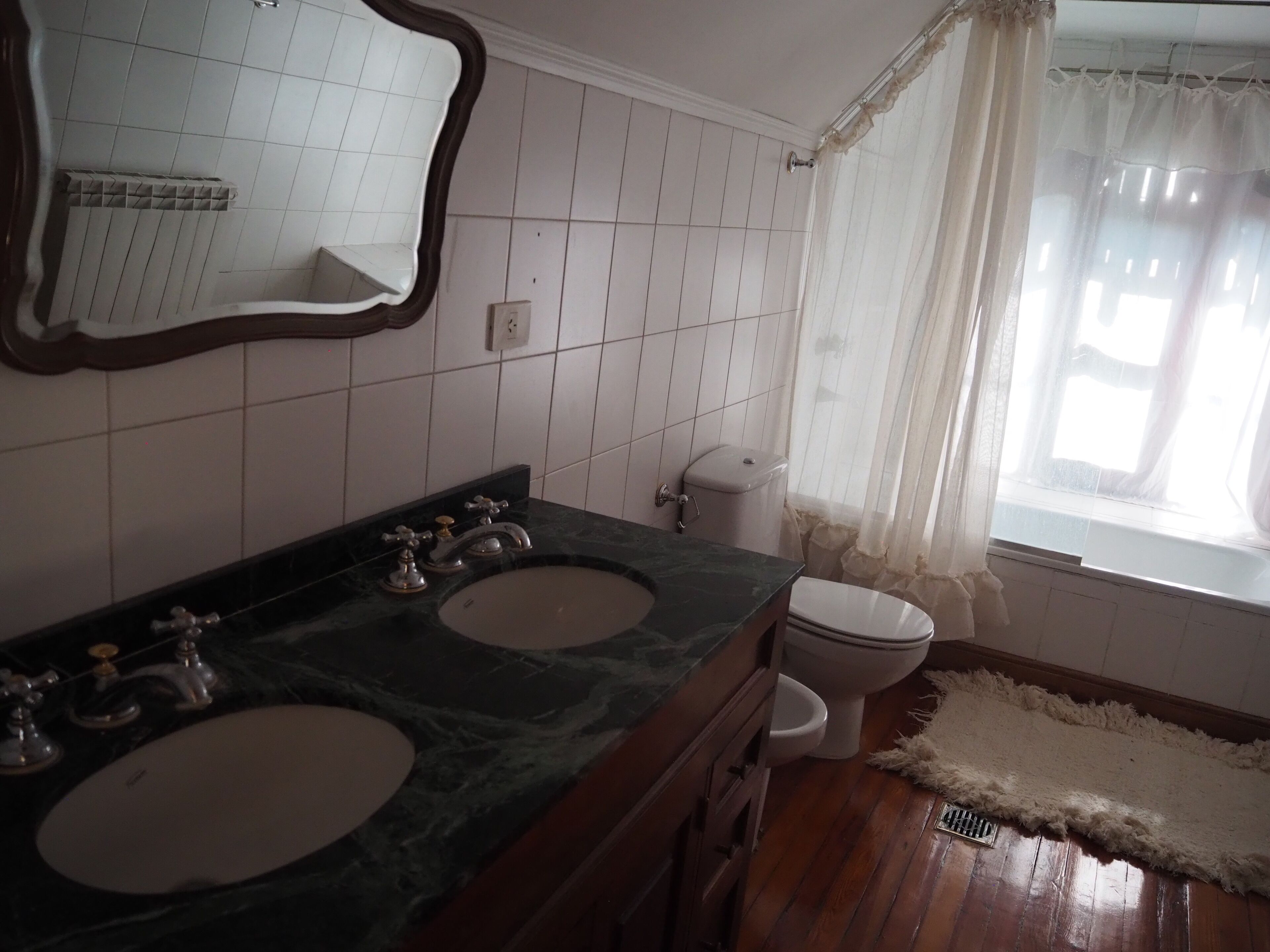 Een badkamer met twee wasbakken, een toilet en een raam met gordijn.