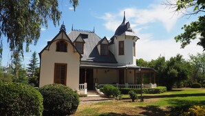 A large, white, two-story house with a steeply pitched roof, a prominent tower, and a covered porch. - Villa Victoria Lodge (Maipu)