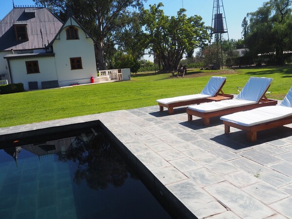A swimming pool with lounge chairs and a house in the background.