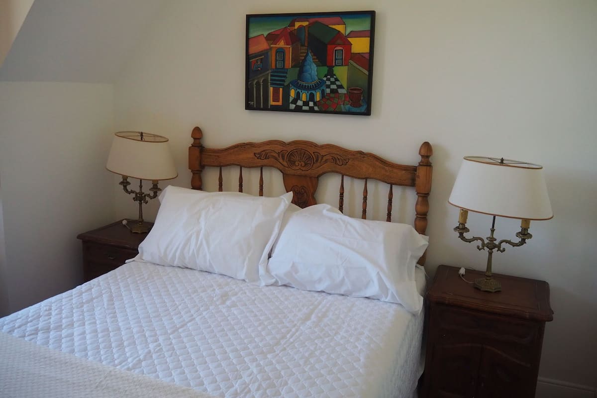 A neatly made bed with white linens, a wooden headboard, and two bedside lamps on matching nightstands.