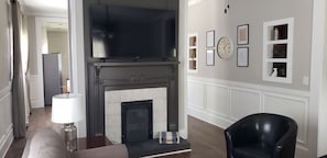 A living room with a fireplace, a black leather chair, a lamp, and framed pictures on the wall.