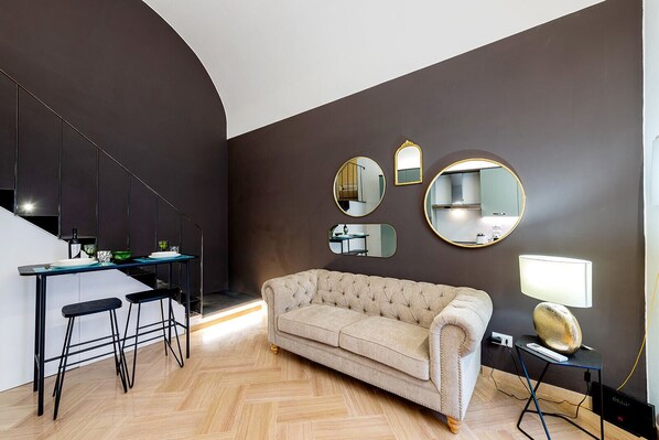 Un salon moderne avec un canapé, un coin repas comprenant une table et des chaises, et une cuisine visible à travers une arche.
