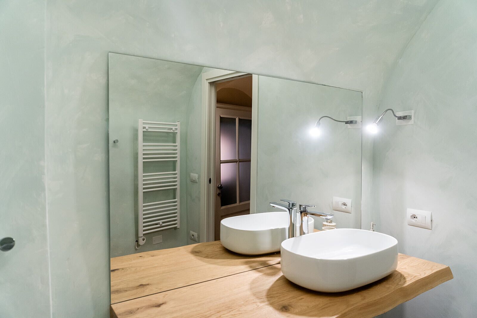 A bathroom with two round sinks, a wooden countertop, a mirror, and a towel rack.
