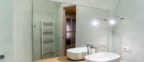 A bathroom with two round sinks, a wooden countertop, a mirror, and a towel rack.