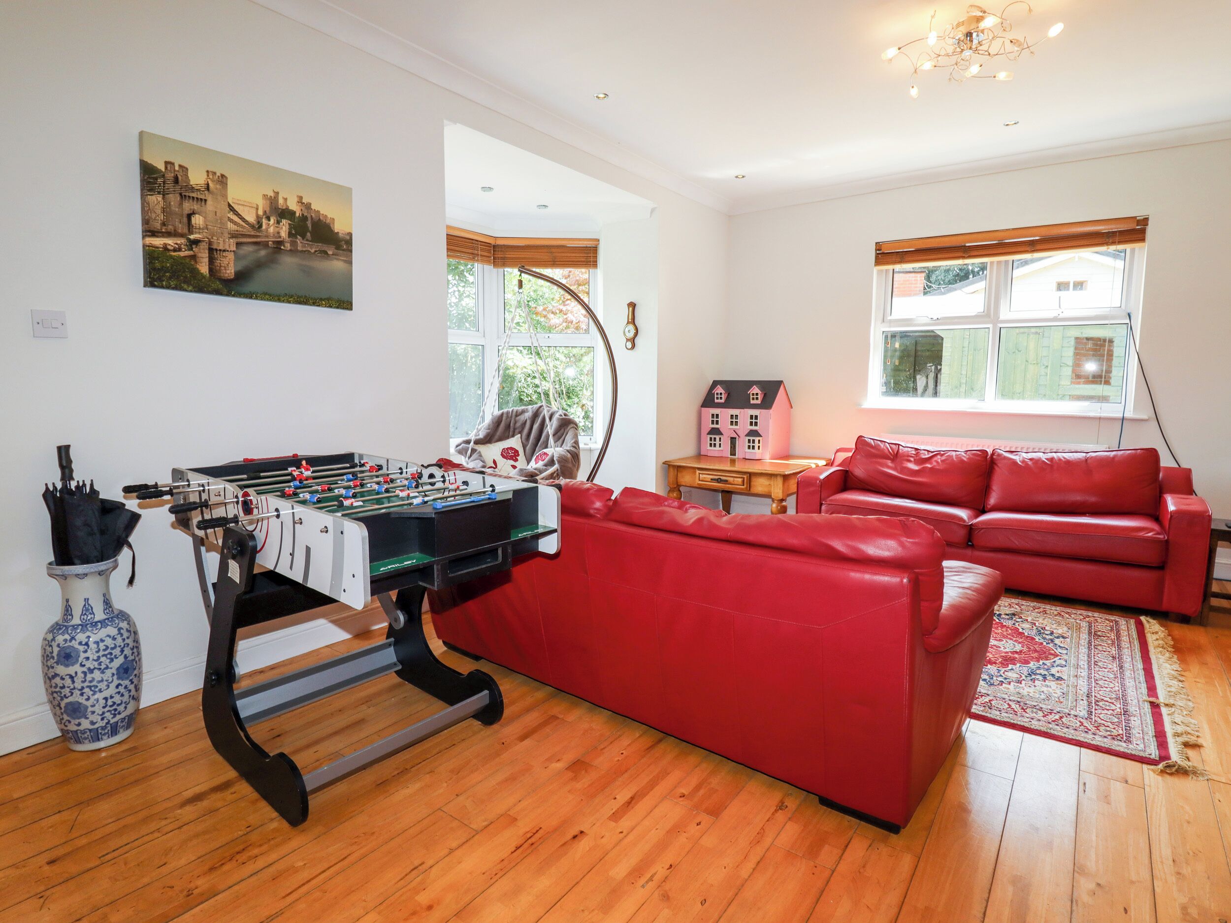 A living room with a foosball table, red leather sofa, and a small house model on a table.