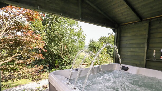 Boblebad med flere jets, omgivet af en træterrasse og udsigt til træer og grøn vegetation.