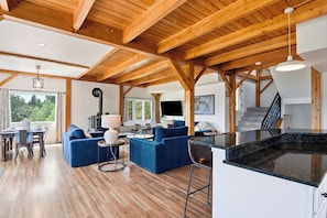 A spacious living area with a wooden ceiling, a dining setup, and a kitchen with a black countertop.