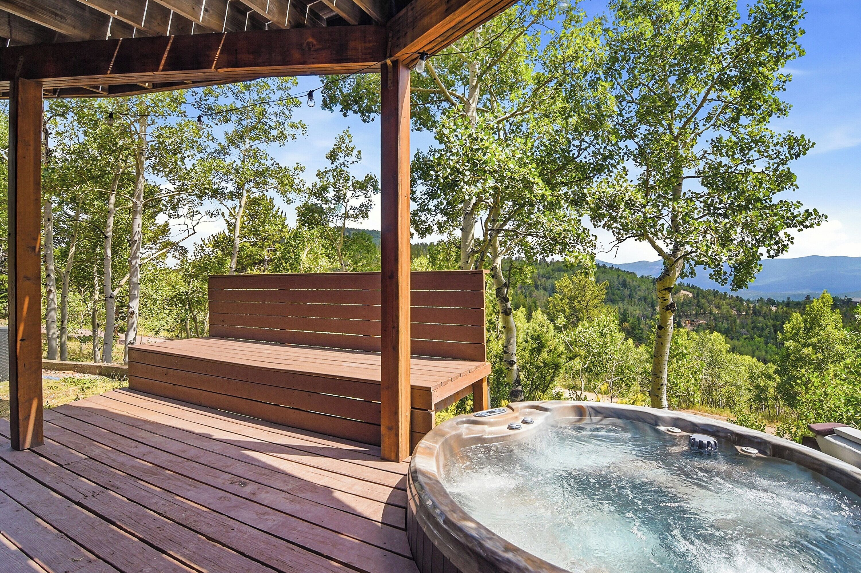 A wooden deck with a hot tub and a bench overlooking a forested area.
